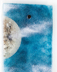 Details of fused glass wall panel featuring a Cornish lighthouse design with a teal blue background and full moon design. 