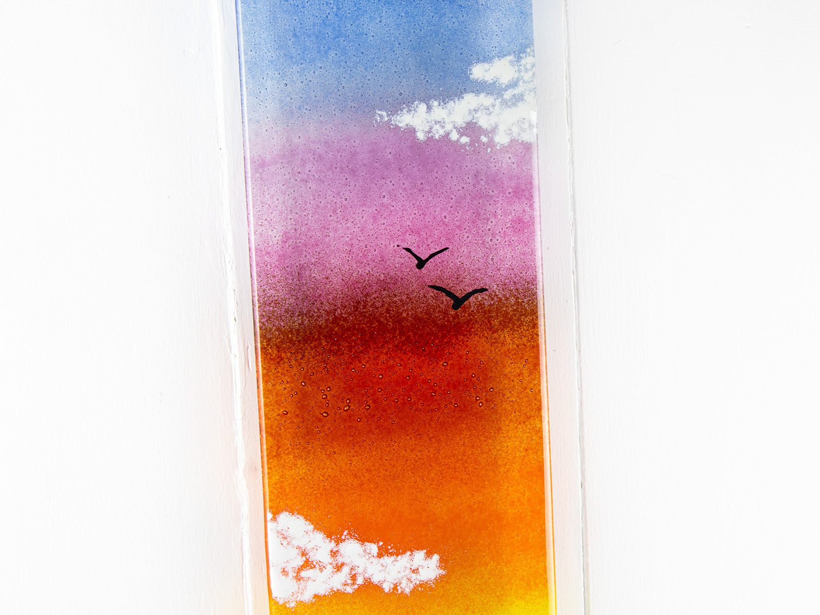 Close up of a fused glass wall panel, featuring a Cornish lighthouse design with a sunset sky and soaring gulls. 