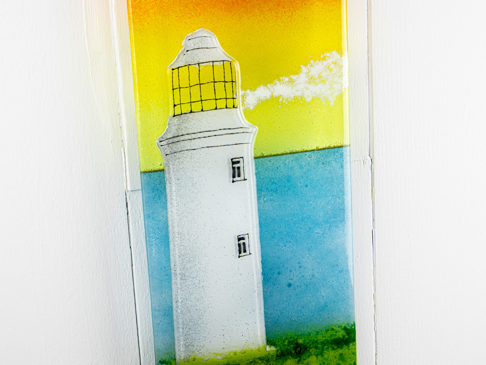 Details of fused glass wall panel, featuring a Cornish lighthouse design with a sunset sky. 