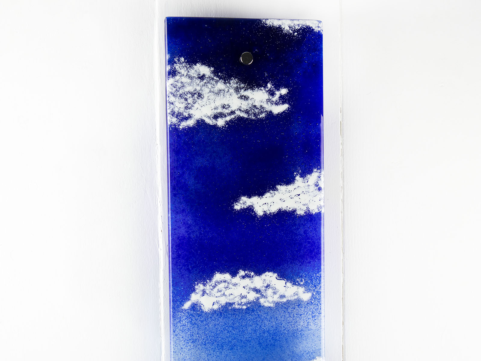 Details of a fused glass wall panel featuring a Cornish lighthouse sat against a coastal blue design.  