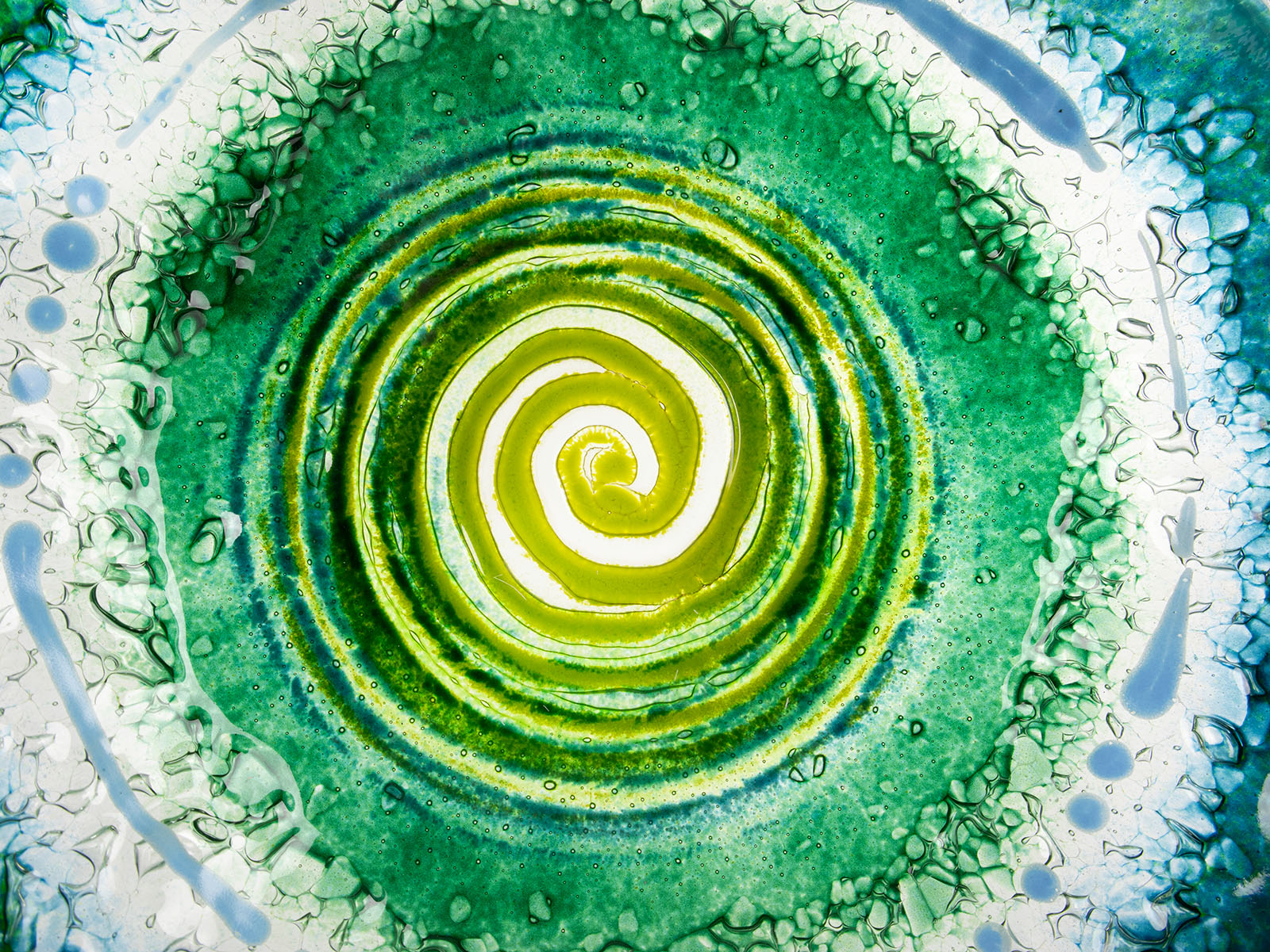 Close up of a fused glass round dish, featuring a dark emerald colour-way and a textured swirling detailing. 
