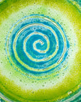 Close up of fused glass round dish featuring bright sea greens and swirling aqua detailing. 