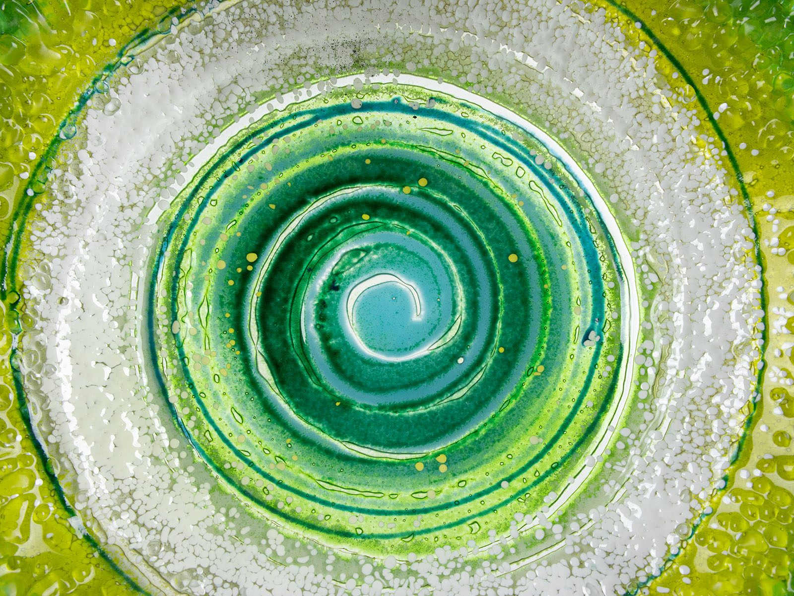 Close up of fused glass round dish in emerald green colours and organic swirling details.