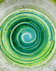 Close up of fused glass round dish in emerald green colours and organic swirling details.