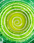 Close up of fused glass round dish, featuring an emerald green colour-way and swirling design. 