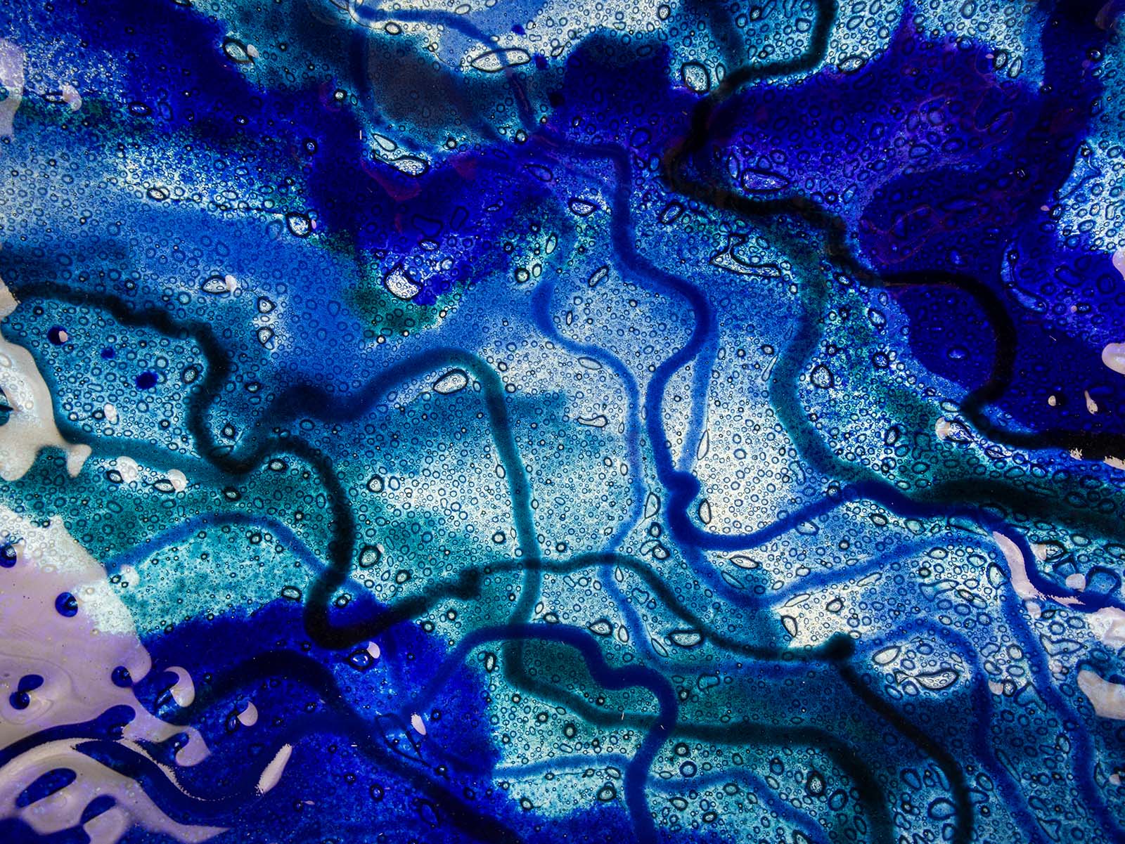 Close up of a fused glass round dish, featuring ocean blue colours and organic detail. 