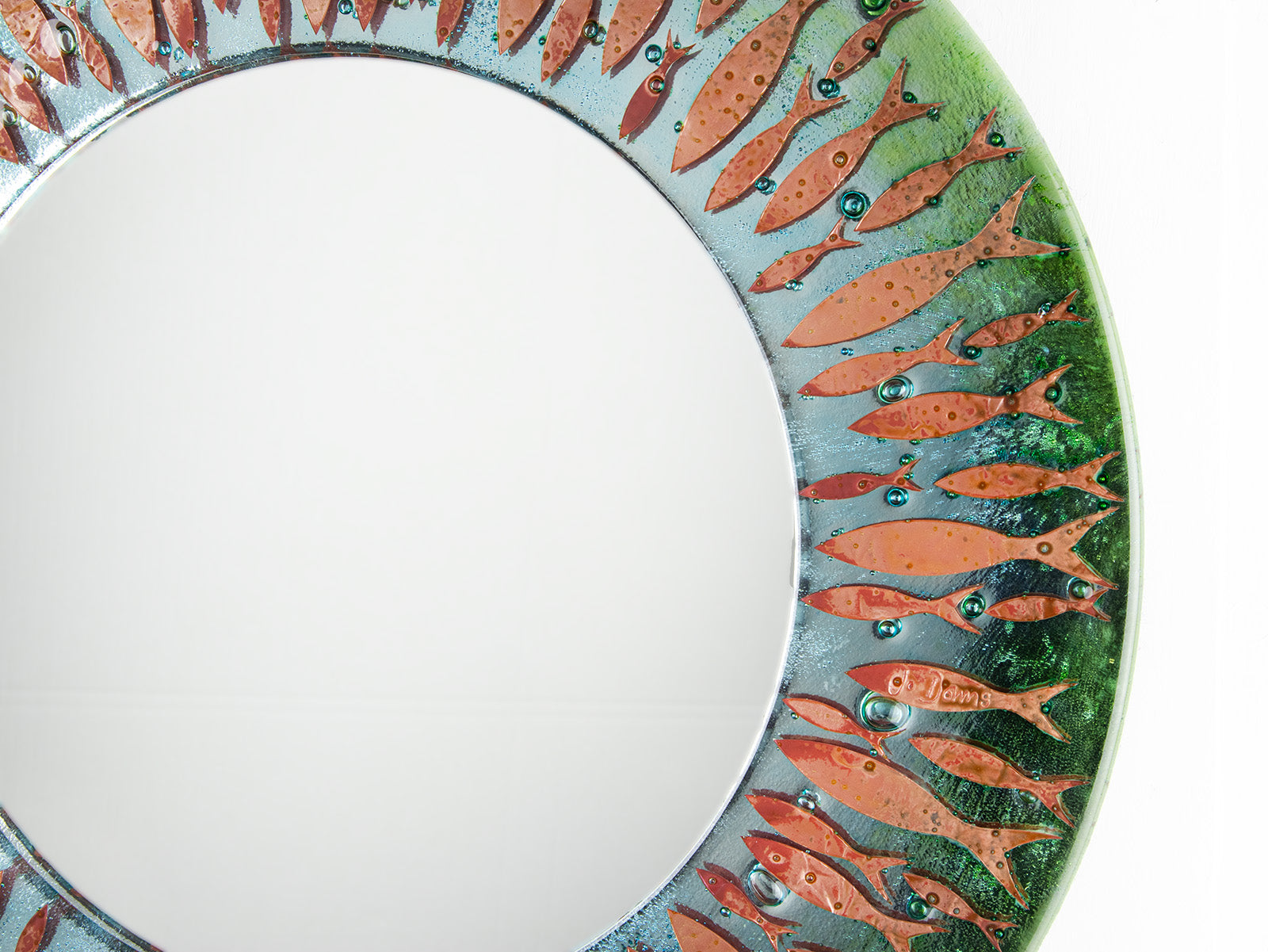 Details of fused glass round mirror featuring a soft, coastal colour-way with copper fish, creating an ocean inspired piece of wall art.