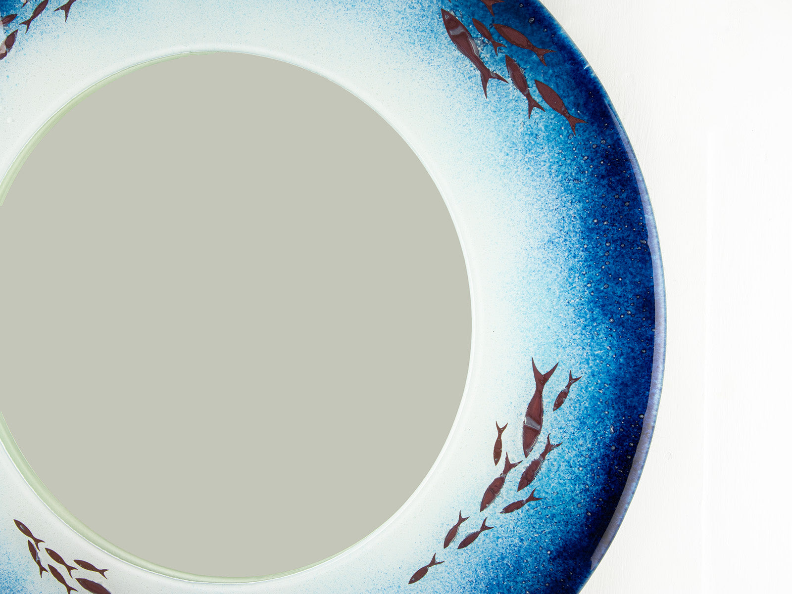 Close up of fused glass round mirror made in coastal blues and copper fish.