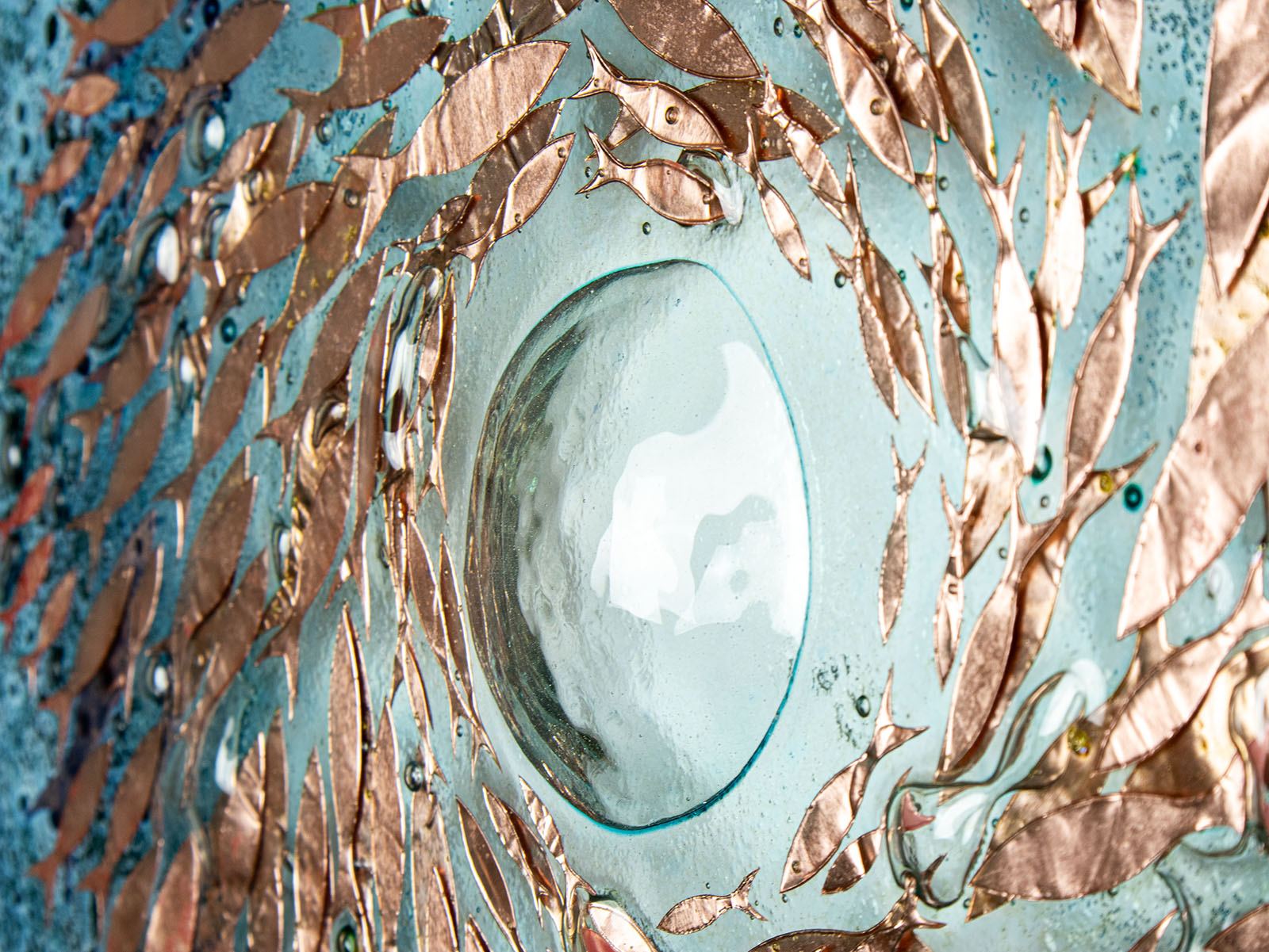 Detail of giant bubbled on a fused glass round panel with copper fish and teal blue design. 