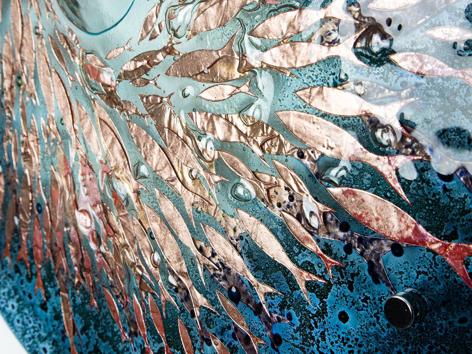 Close up of copper fish on a teal blue round fused glass panel. An ocean inspired wall art design. 