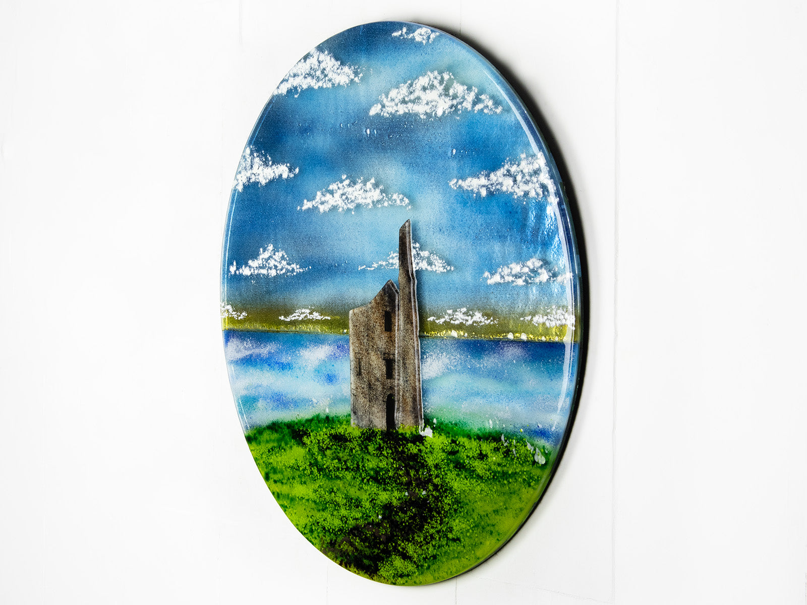 Side on image of fused glass round wall panel, featuring Cornish Tin Mine, in coastal design. 