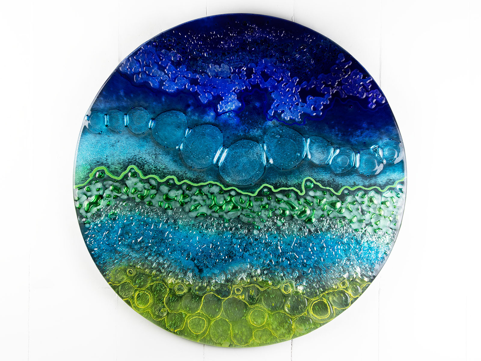 Fused glass round wall panel in an abstract ocean inspired design with textured detail. 