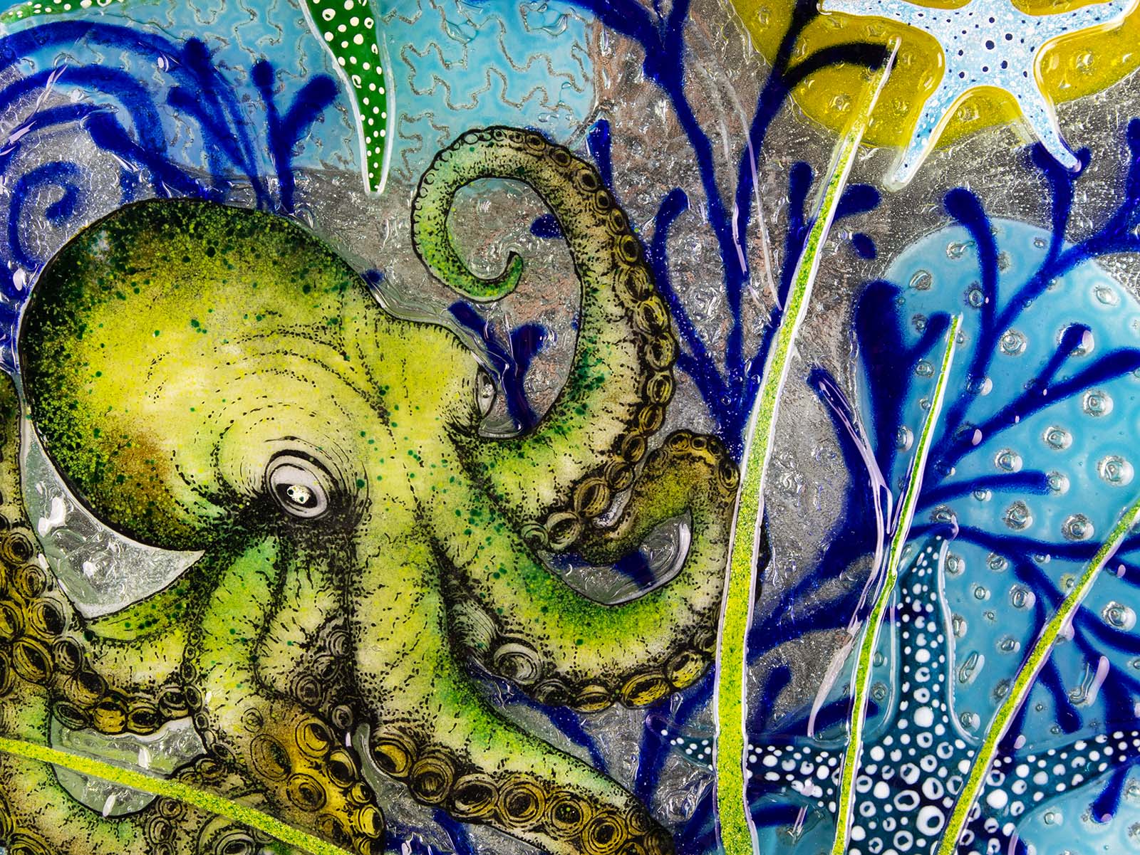 Close up image of a fused glass round wall panel with a green octopus design, hand-painted with organic, textured detail. An ocean reef inspired piece of wall art. 