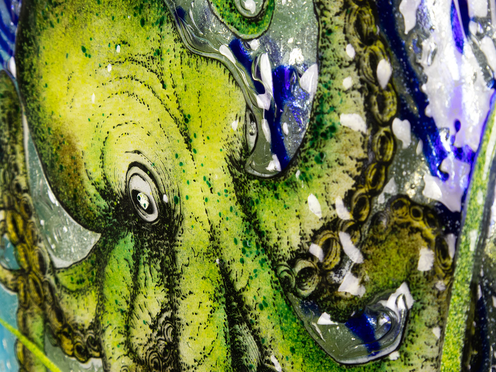 Details of a hand-painted green octopus with intricate detailing on a fused glass round panel. 