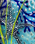 Close up of a blue starfish on a fused glass round panel in coastal colours.