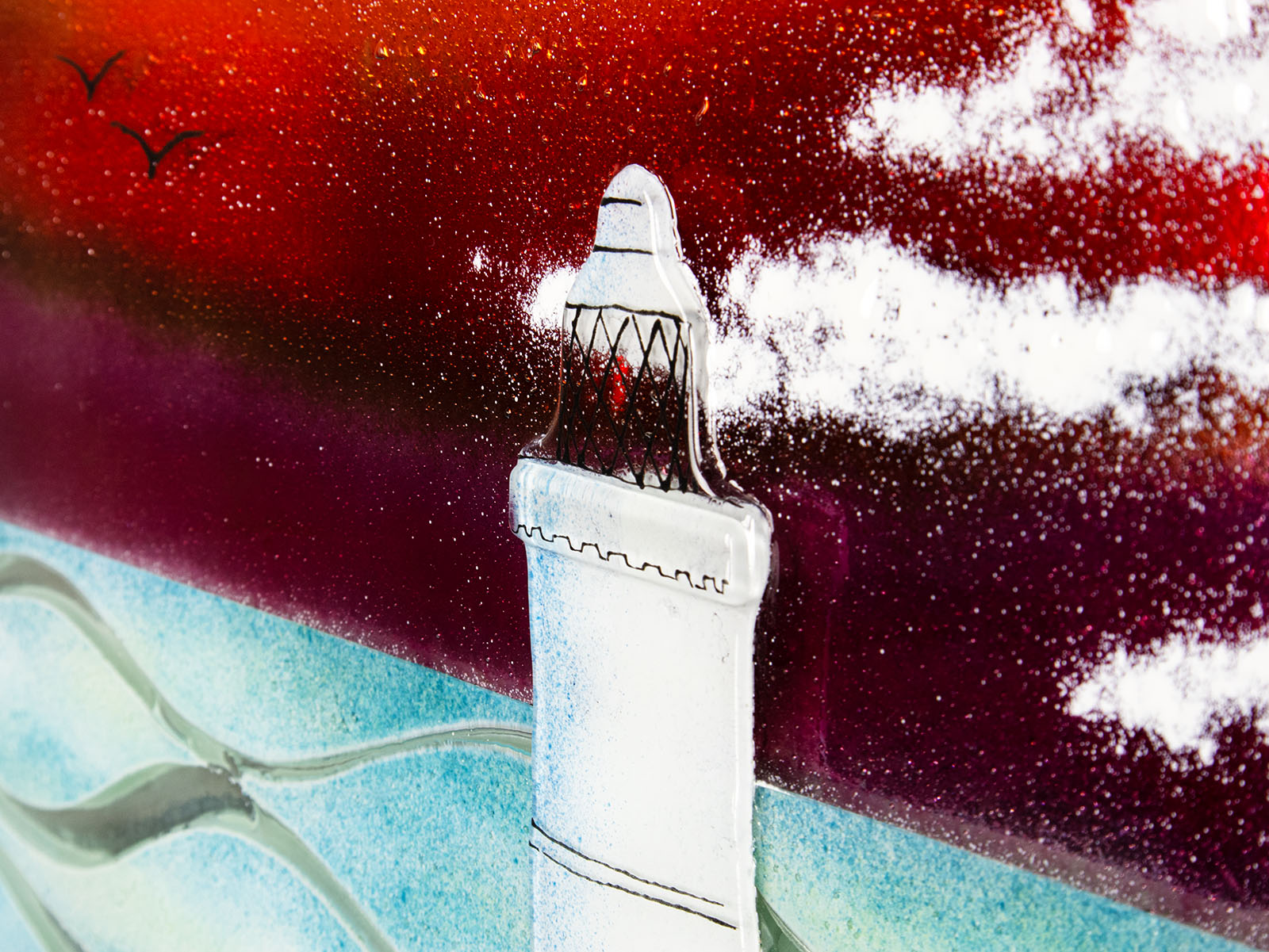 Close up of a lighthouse with a sunset sky on a fused glass panel, with soaring seagulls. 