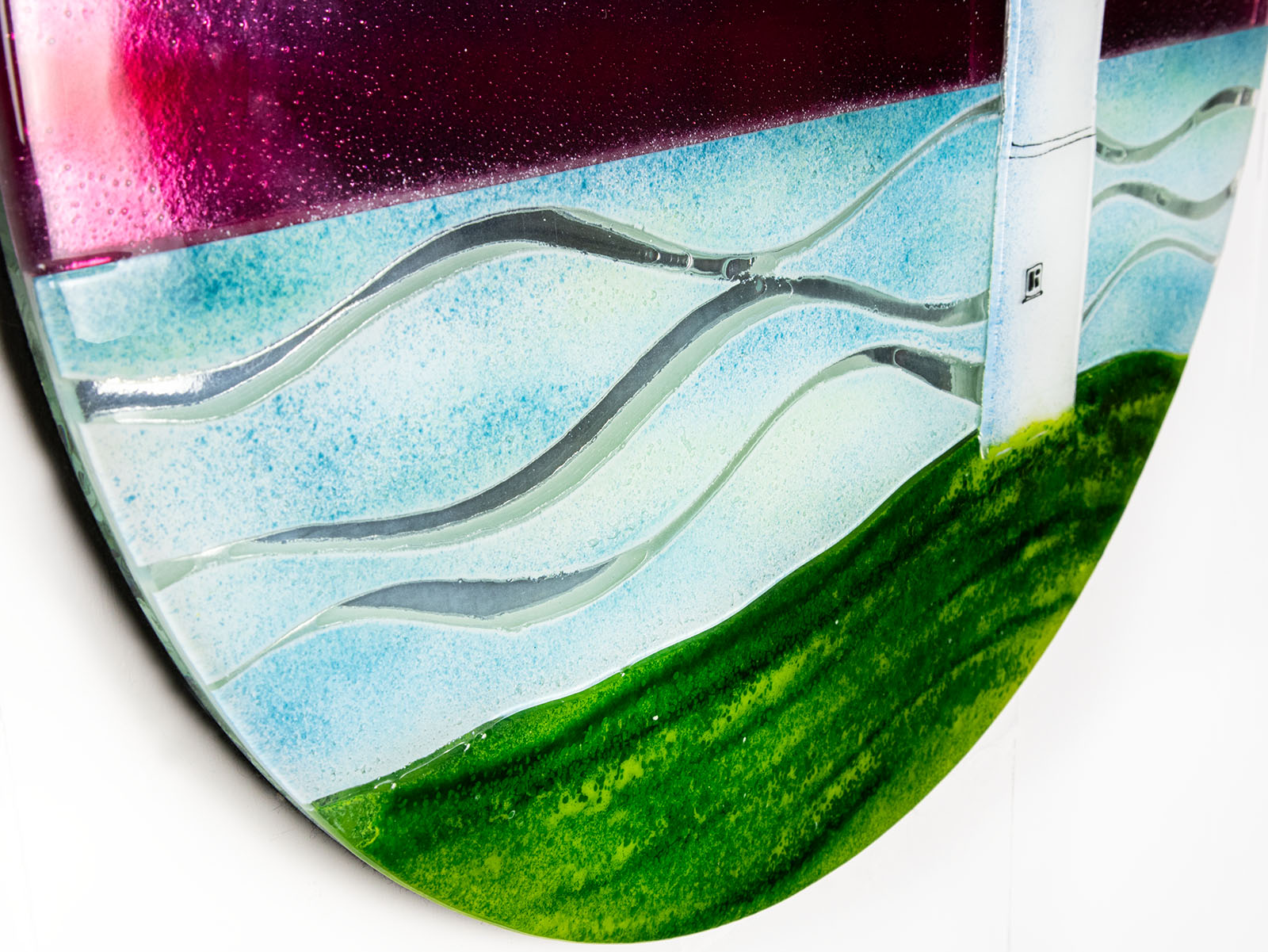 Wave details on a fused glass round panel inspired by a lighthouse on a coast-path with a sunset sky. 