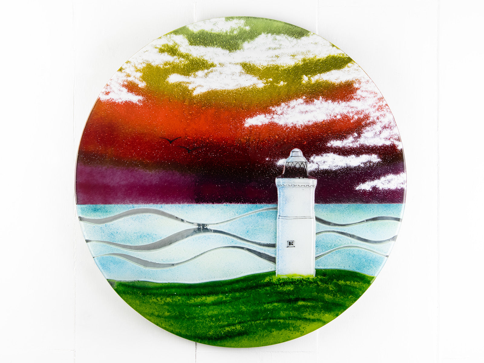Fused glass round panel with a lighthouse deign and a vibrant coastal colour-way.