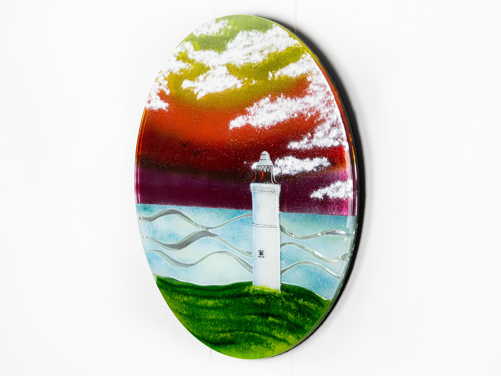 Fused glass round panel with a lighthouse design and sunset sky.