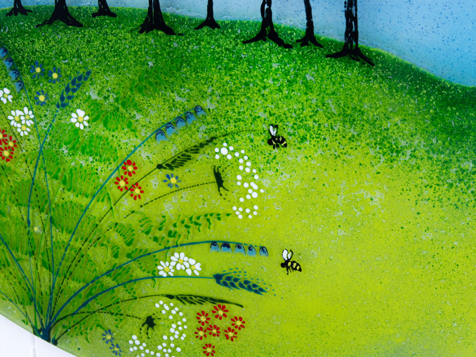Close up of hand-painted bees and flowers on a fused glass round panel, inspired by the Nearly Home Trees in Devon, designed in bright summer greens. 