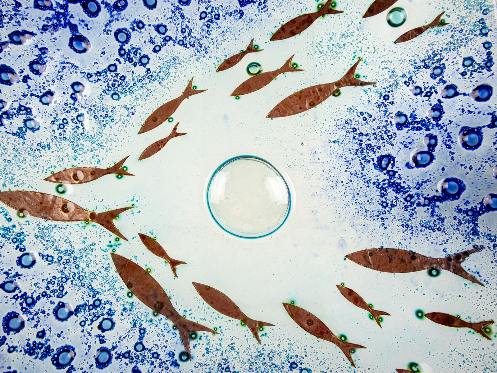 Close up of design on fused glass square dish, handmade in coastal blues, with copper fish. 