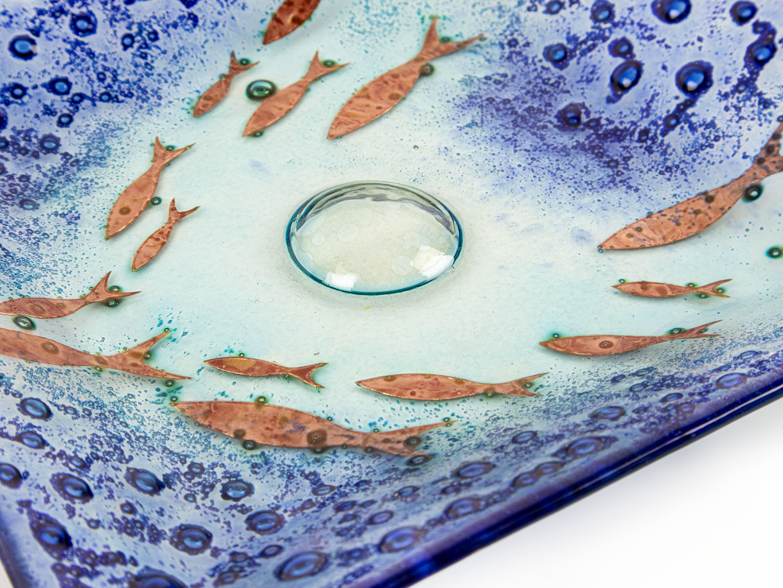Bubbled detail of fused glass square dish, handmade in coastal blues, with copper fish. 