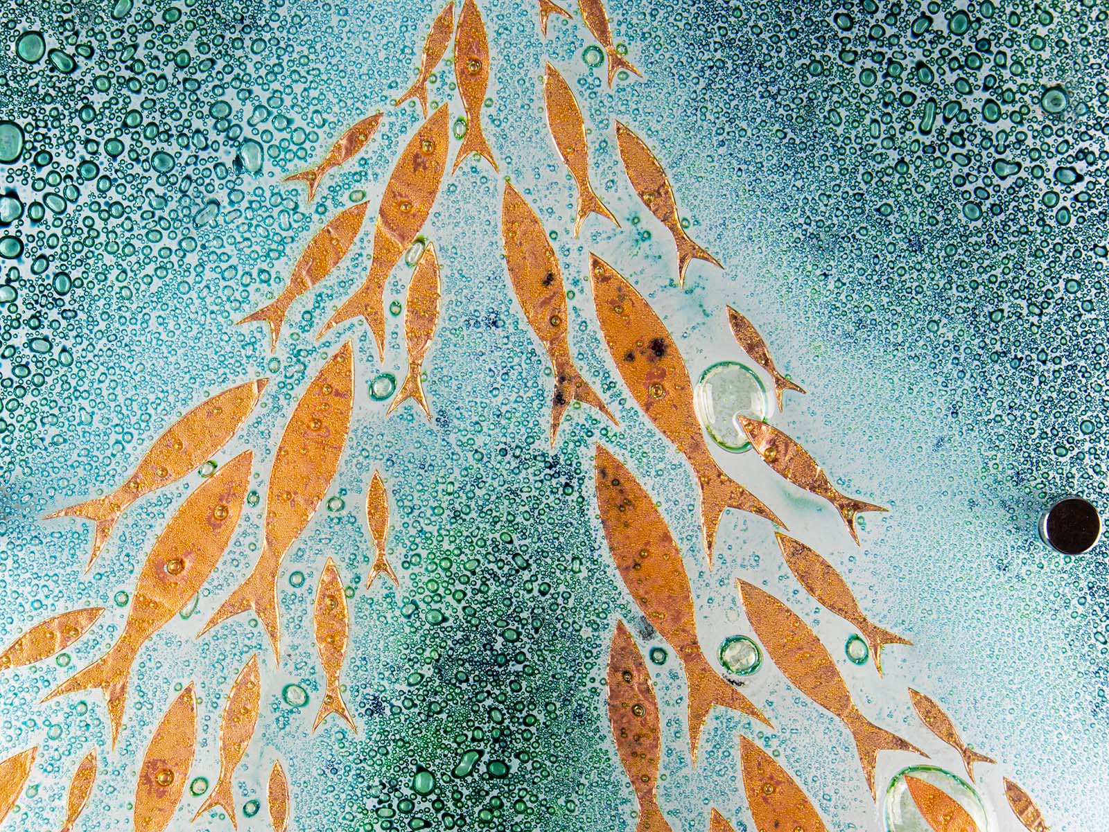 Close up of fused glass square wall panel, featuring sea green colours and copper fish detailing. 