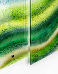Close up of a fused glass triptych with emerald green colours in an organic, ocean inspired design. 