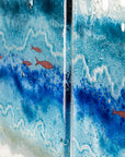 Copper fish detailing on a fused glass triptych depicting a beach scene with blue water and yellow sand.