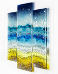 Fused glass triptych depicting a beach scene with blue water, yellow sand, and red, copper fish.