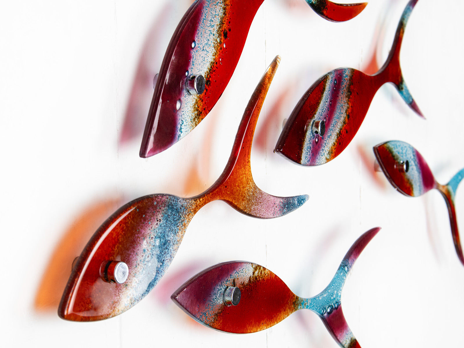 Close up o fused glass shoal of fish in bright reds and aqua hues, with shadows.