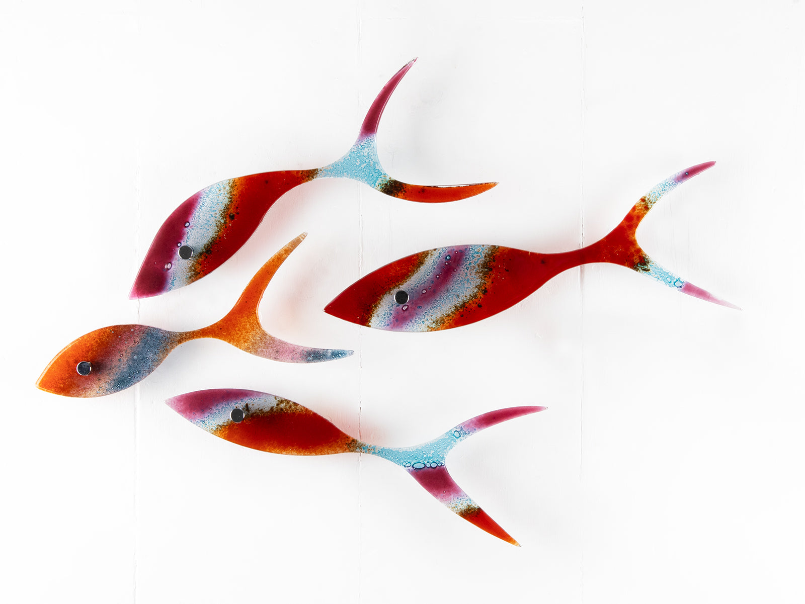 Fused glass shoal of fish in bright reds and aqua hues. 