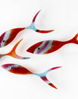 Fused glass shoal of fish in bright reds and aqua hues. 
