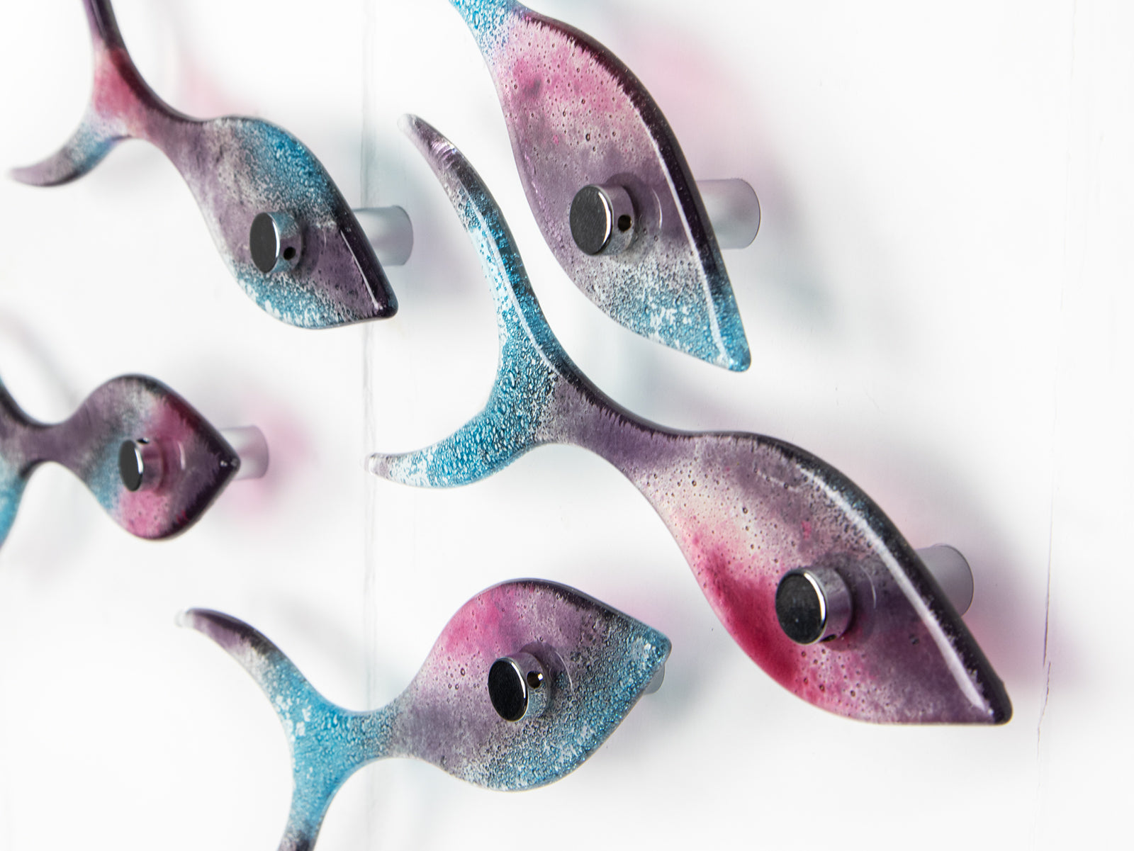 Close up of fused glass shoal of fish on a wall, handmade in bright pinks and coastal blues.