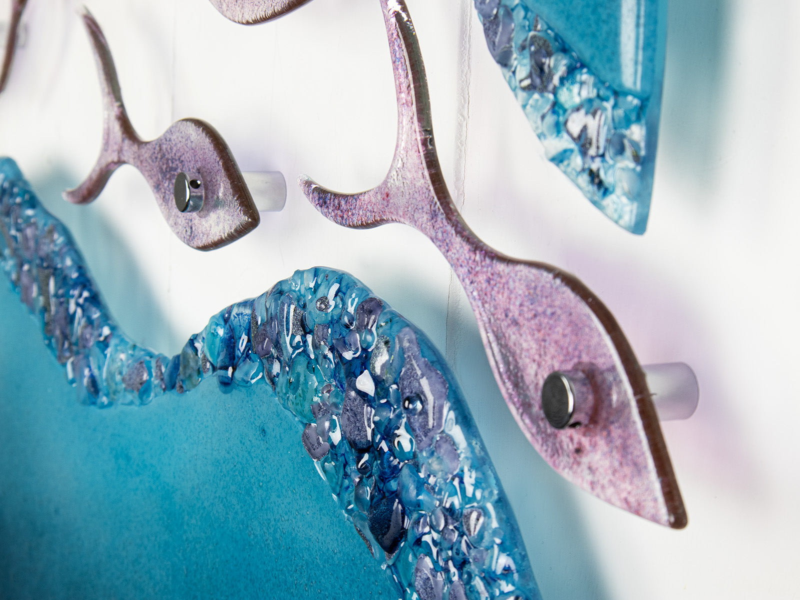 Close up of glass fish on a fused glass wall art display with shoal of fish and coastal blue colours. 