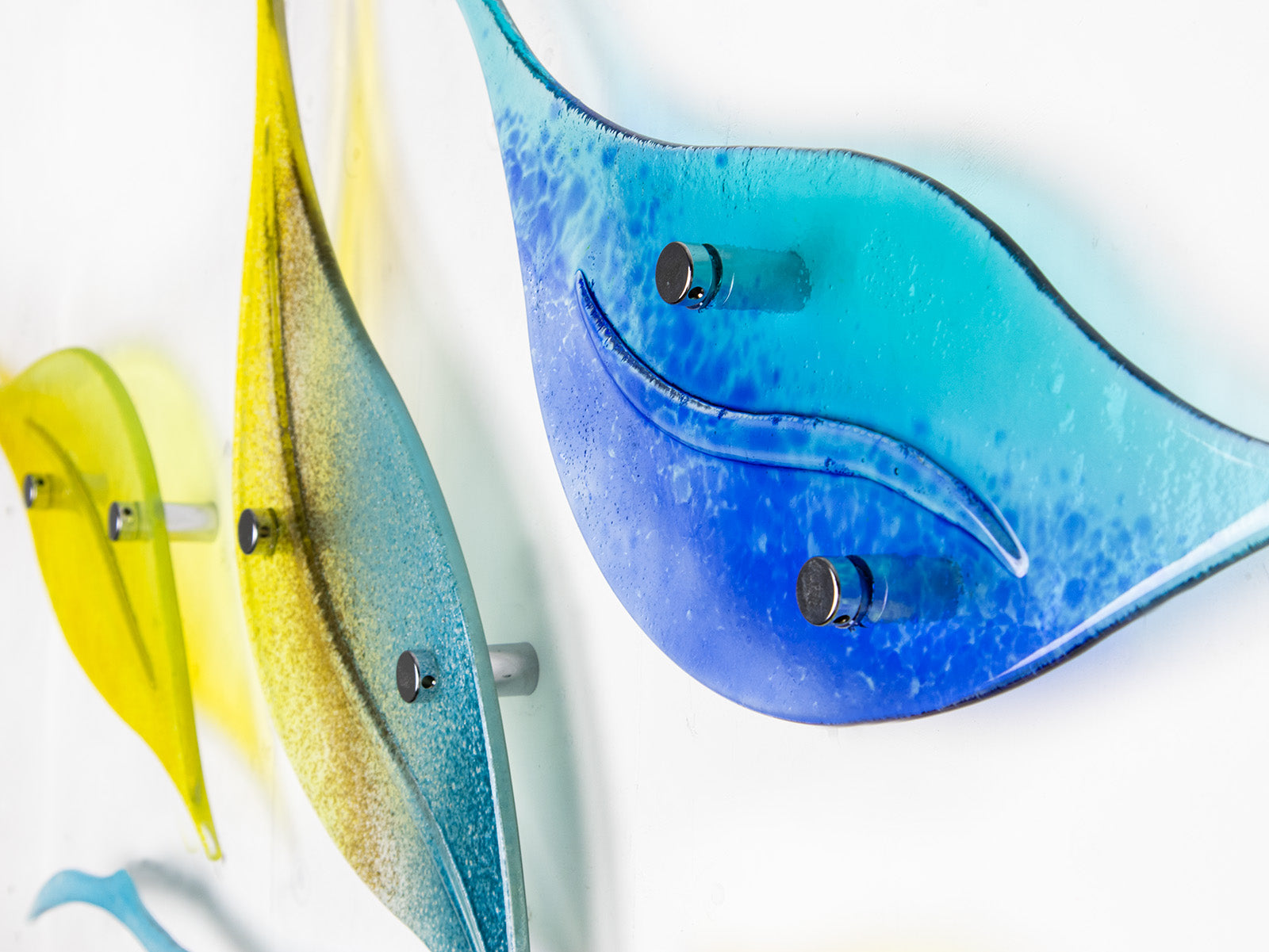 Close up of fused glass leaf wall art display in bright yellows and sky blues. 