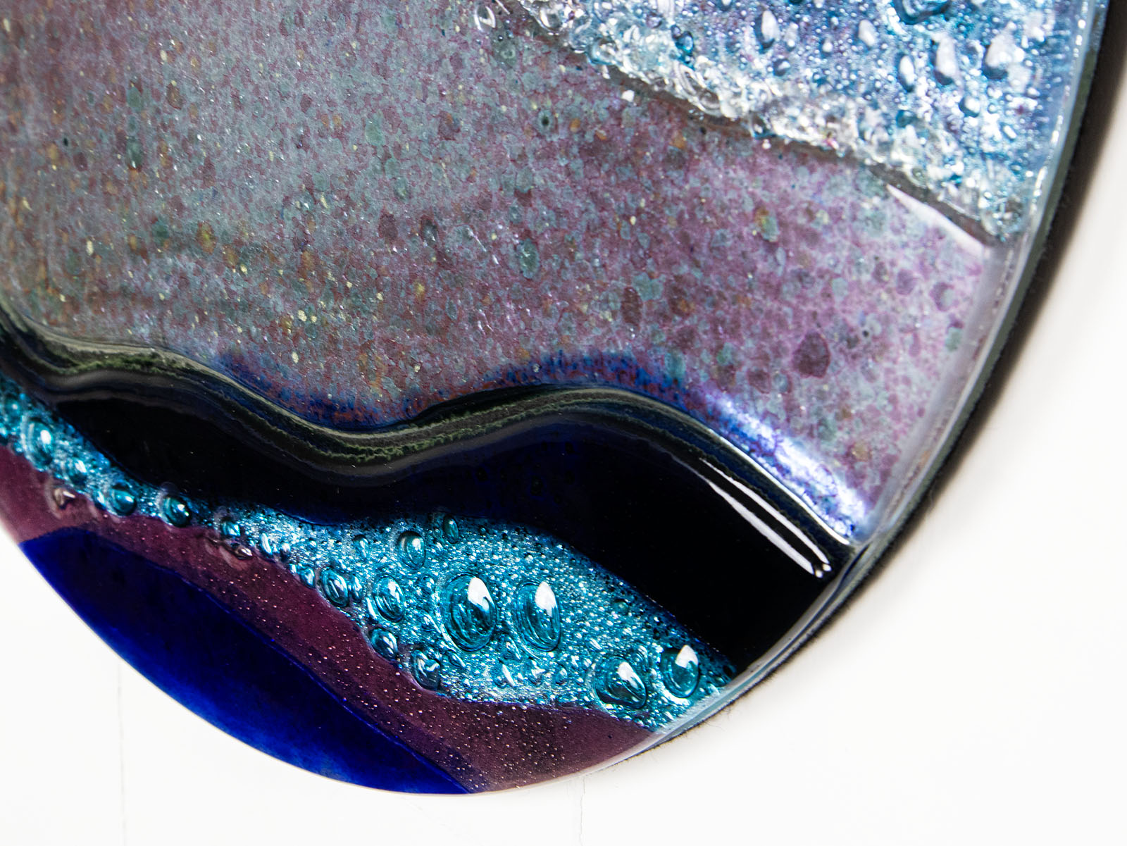 Close up of abstract fused glass round panel, with wavy design in ocean purple colours and texture. 