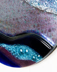 Close up of abstract fused glass round panel, with wavy design in ocean purple colours and texture. 