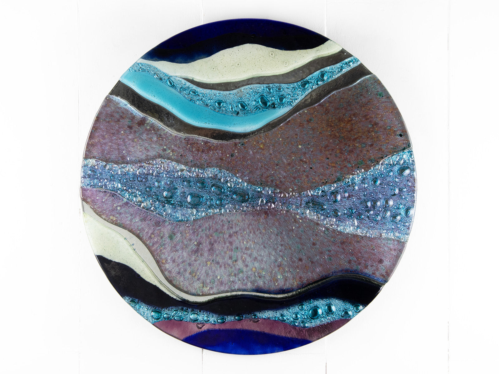 Abstract fused glass round panel, with wavy design in ocean purple colours and texture. 