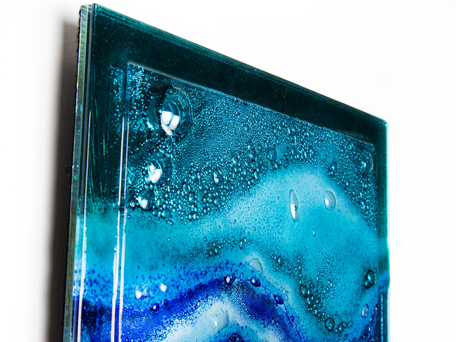 Close up of abstract and bright fused glass wall panel, inspired by the ocean with coastal colours and bubbled detailing. 