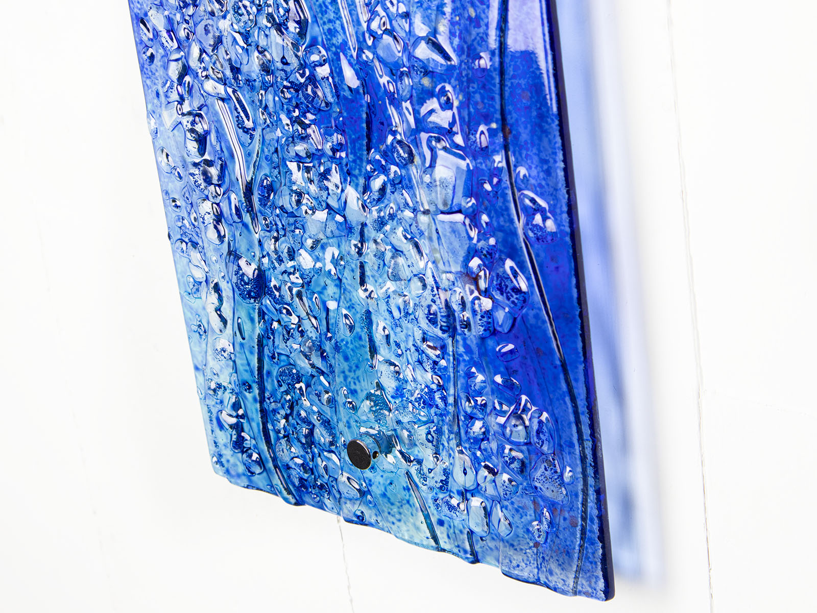 Close up of the texture on a fused glass ocean inspired wall panel with texture and bright blues.