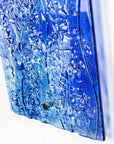Close up of the texture on a fused glass ocean inspired wall panel with texture and bright blues.