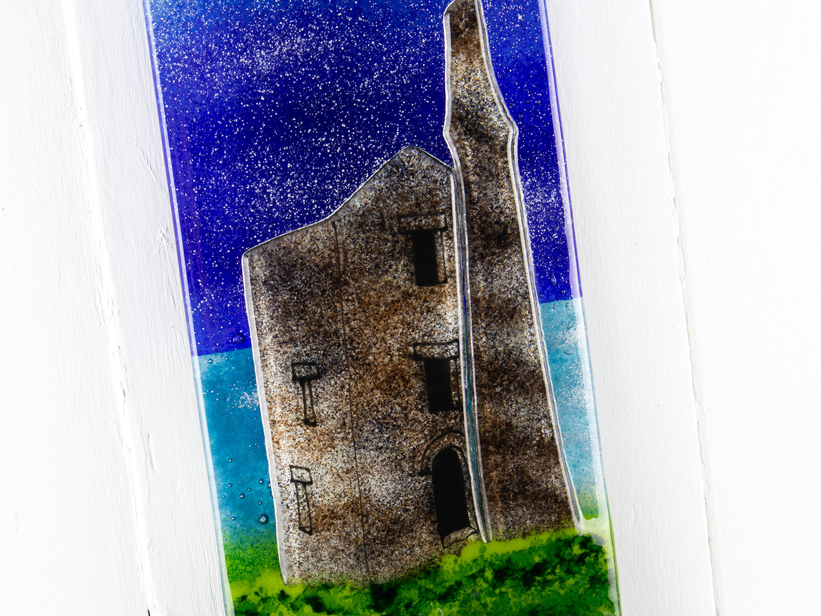 Details of small fused glass wall panel, featuring a Cornish tin mine design, with a coastal moonlight sky. 