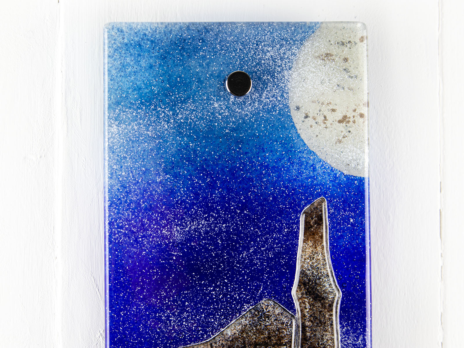 Close up of small fused glass wall panel, featuring a Cornish tin mine design, with a coastal moonlight sky. 