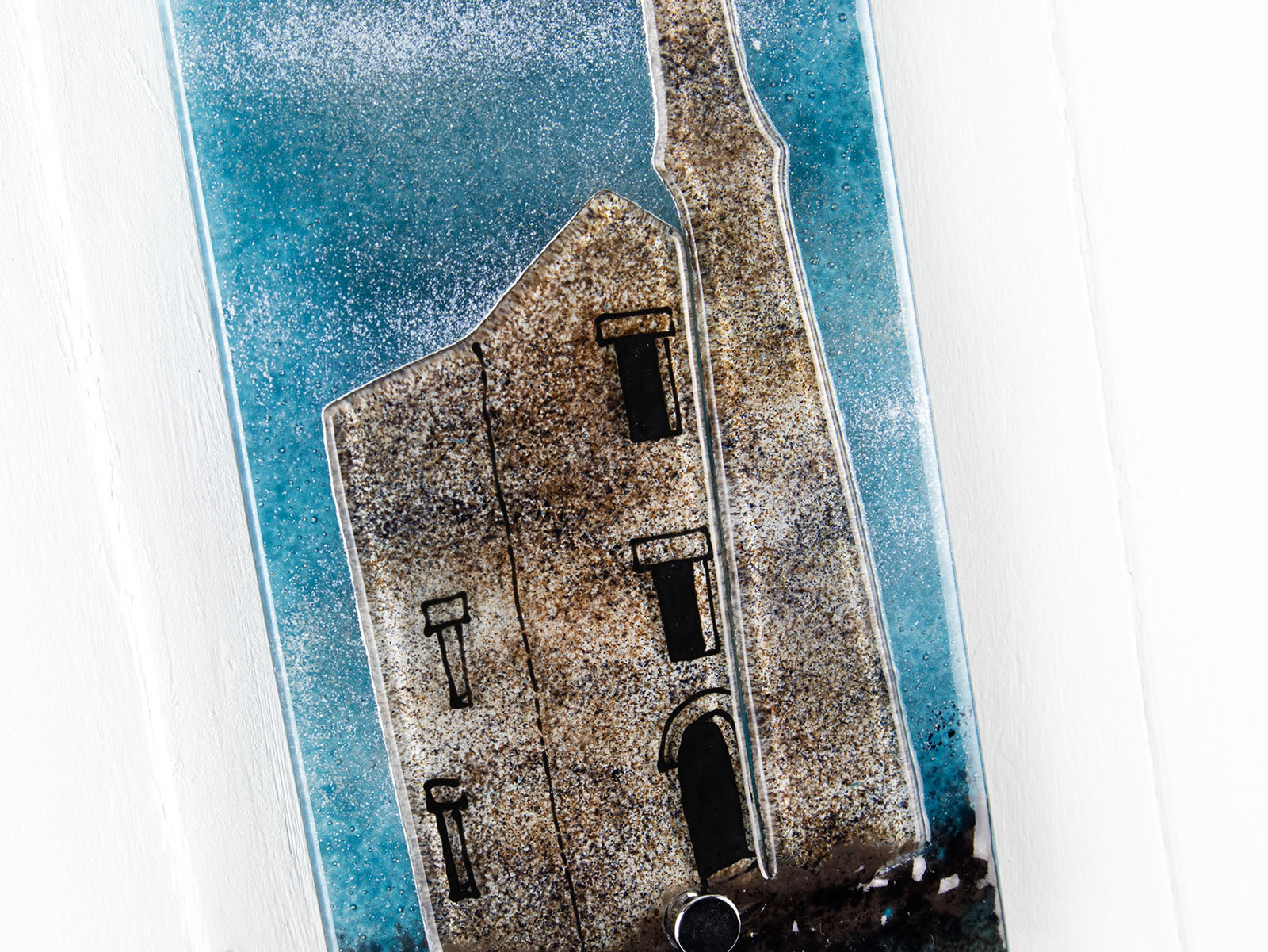 Close up of small fused glass wall panel featuring a Cornish tin mine design, with a misty blue sky. 