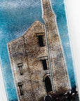 Close up of small fused glass wall panel featuring a Cornish tin mine design, with a misty blue sky. 