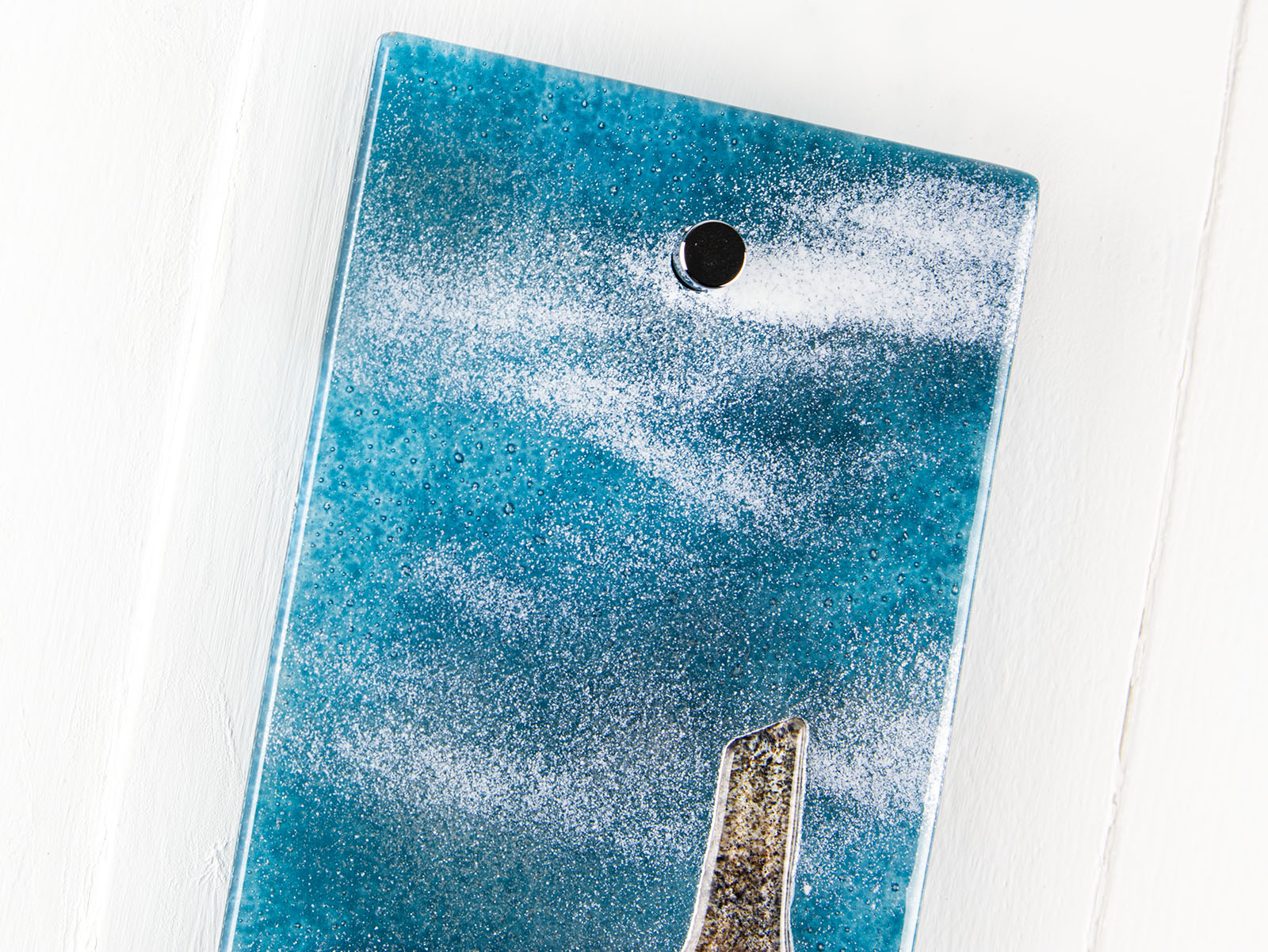 Details of small fused glass wall panel featuring a Cornish tin mine design, with a misty blue sky. 