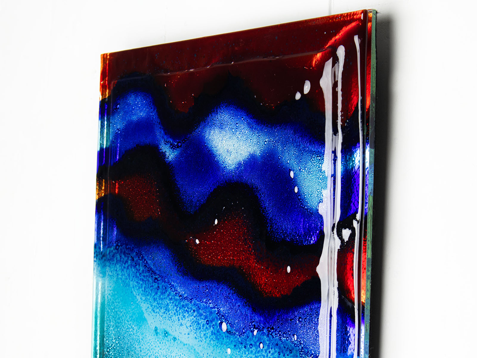 Close up of abstract and bright fused glass wall panel, inspired by the atmosphere of the ocean, with coastal colours and bubbled detailing. 