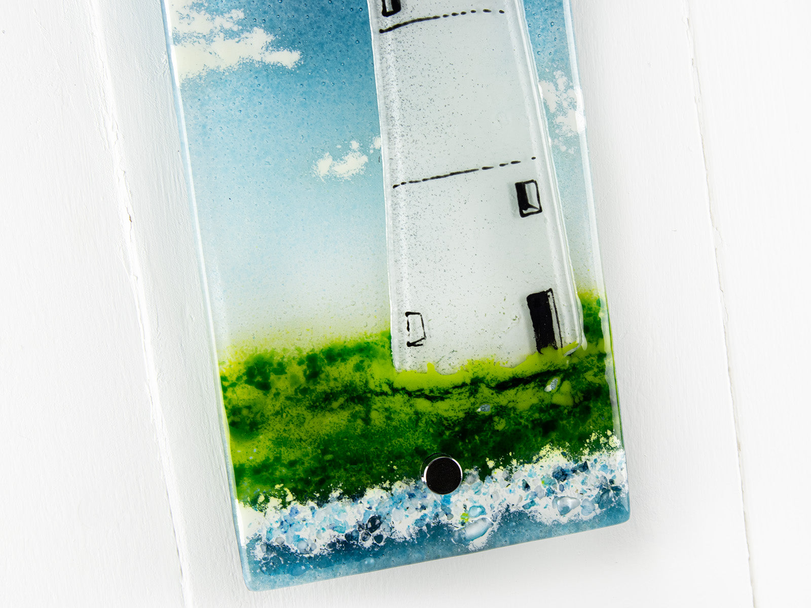 Details of a fused glass wall panel, made with a lighthouse design by the coast. Stunning coastal hues, a stunning hand-made piece of wall art. 