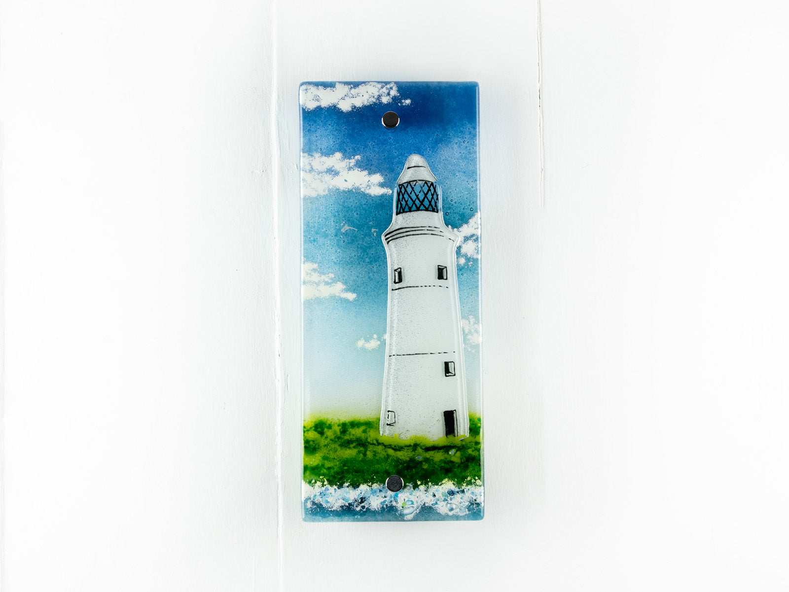 A fused glass wall panel, made with a lighthouse design by the coast. Stunning coastal hues, a stunning hand-made piece of wall art. 